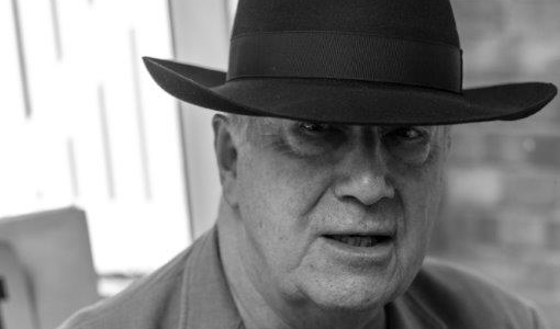 A close up, black & white portrait of John Tilbury, in a large fedora hat