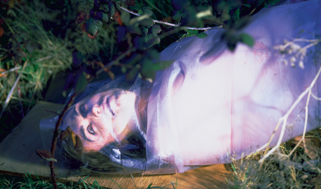 Terre Thaemlitz lies on the ground, wrapped in a plastic sheet, and eerily lit
