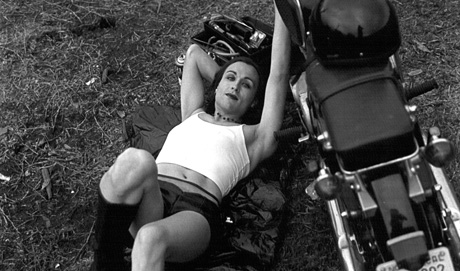 Terre Thaemlitz lies on the ground, next to a motorcycle, posing provocatively