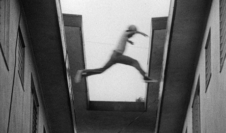 B&W film still of a boy jumping from one roof to another, taken from below