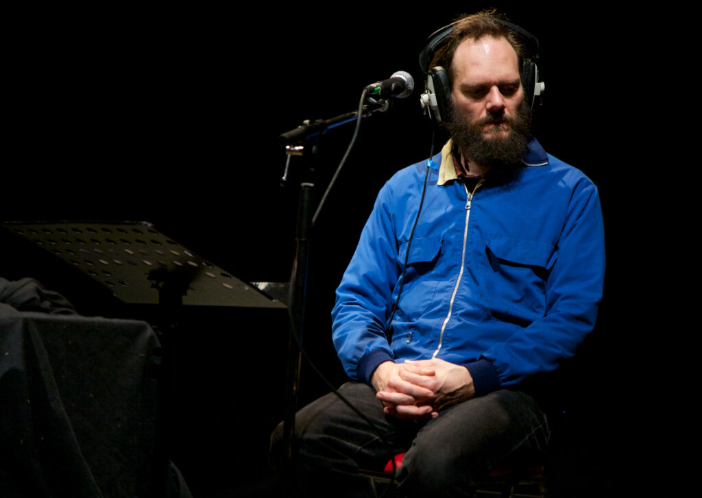 A man in a blue jacket seems to listen intently whilst wearing large headphones