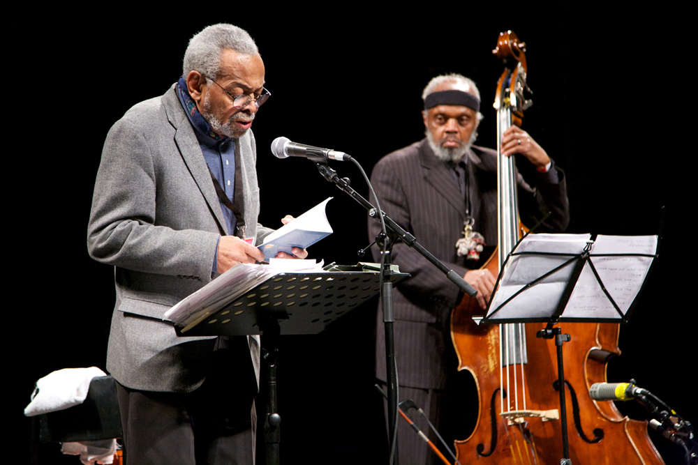 Amiri Baraka reads poetry at a mic and Henry Grimes plays a double bass bass
