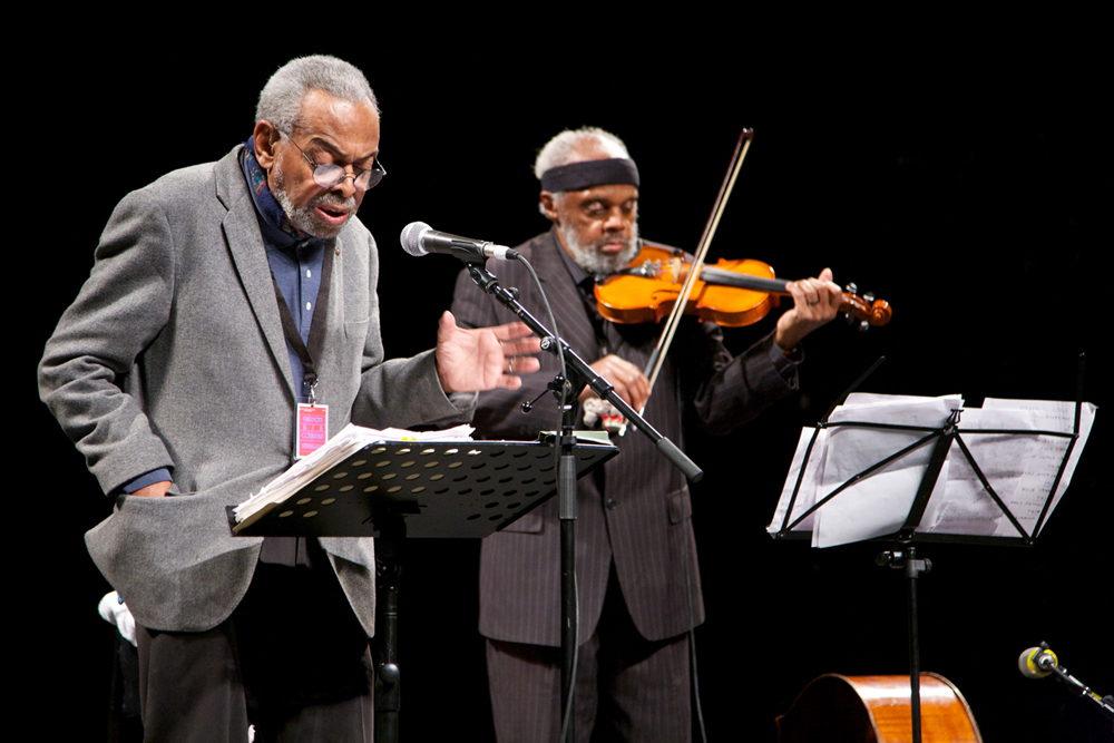 Amiri Baraka reads poetry at a microphone and Henry Grimes plays a violin
