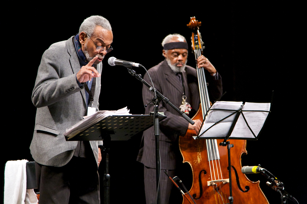 Amiri Baraka reads poetry at a microphone and Henry Grimes plays a double bass