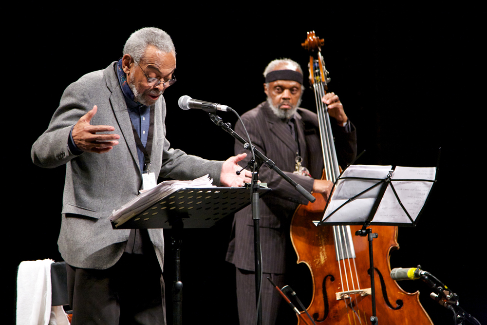 Amiri Baraka reads poetry at a microphone and Henry Grimes plays a double bass