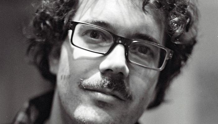 A close up portrait of Alexi Kukuljevic wearing glasses and a moustache