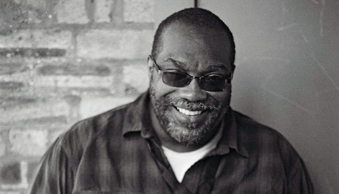 A portrait of Fred Moten wearing sunglasses and a cheeky smile