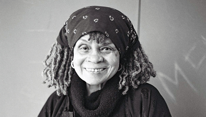 A portrait of Sonia Sanchez she is wearing a head scarf and a broad smile