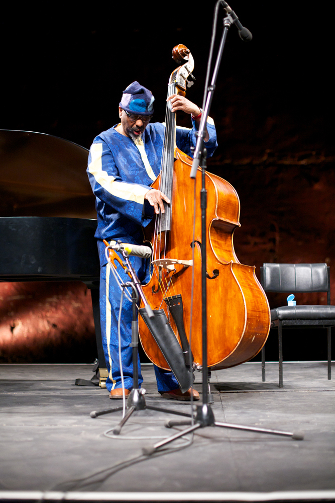 William Parker dressed in blue plays his double bass in a performance space