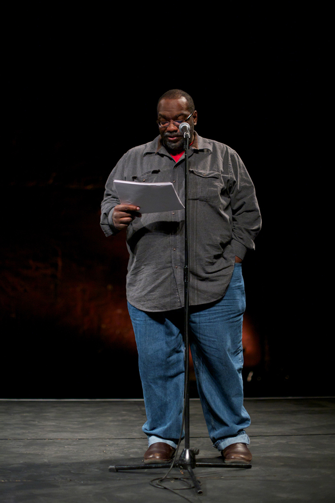 Fred Moten standing at a microphone reading poetry