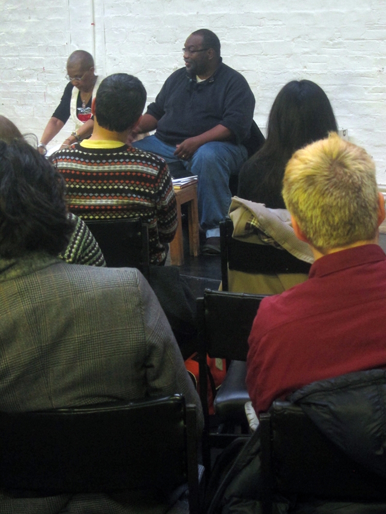 Fred Moten speaks, the shot is taken through two rows of audience members