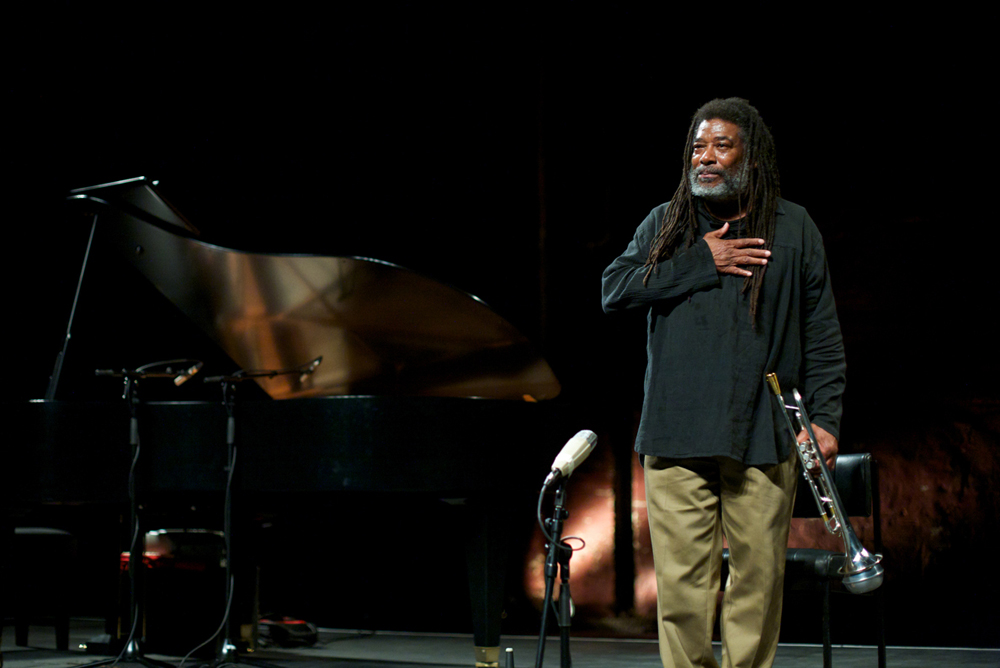 Wadada Leo Smith thanks the audience, hand on his heart, trumpet by his sideide