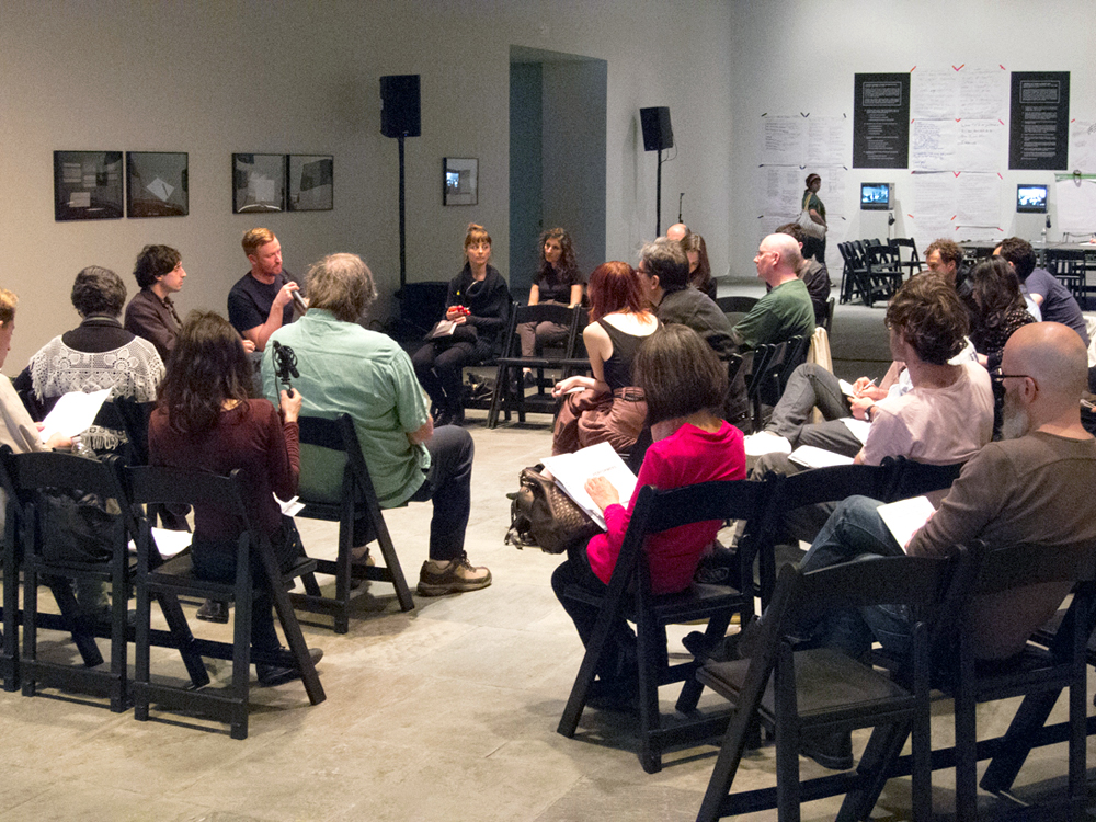 An audience sit around as Barry Esson and Jay Sanders talk in a gallery