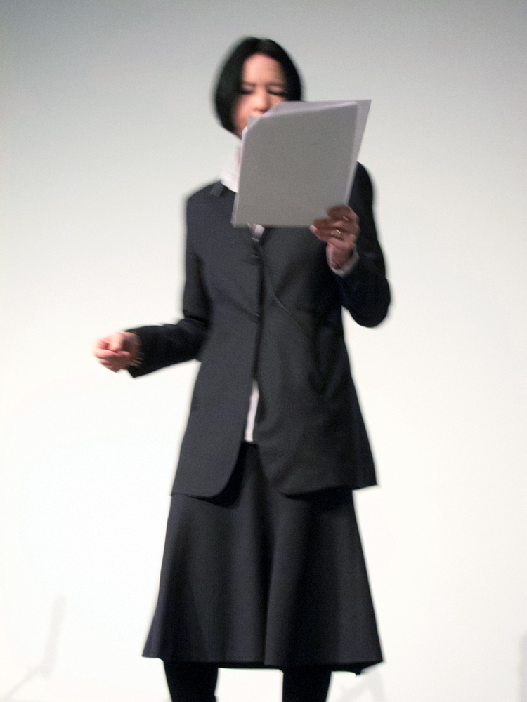 A fuzzy shot of Vanessa Place reading from papers