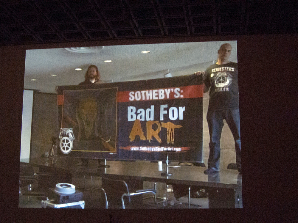 A screen showing two people holding a Sotherbys Bad for Art banner