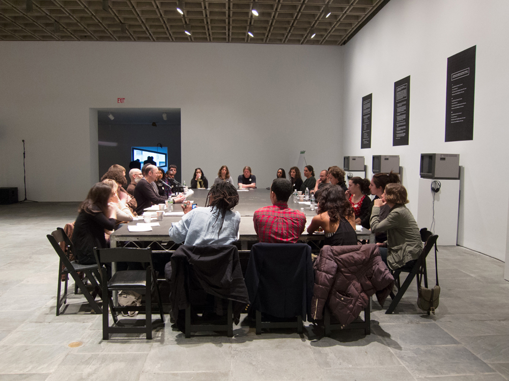 A large group of people sit around a large table in a gallery