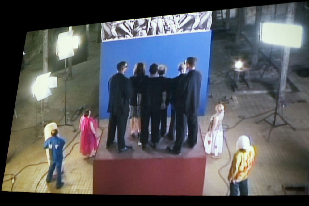 A shot of a screen showing a film by Chto Delat in which a group of people sing