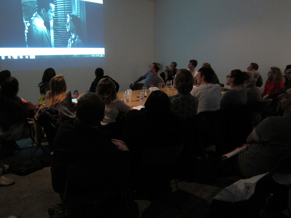 The audience around a large table with a screening on the wall
