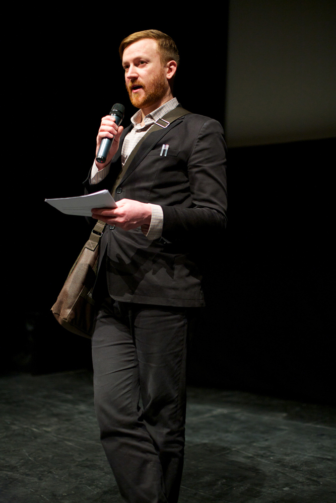 Barry Esson in a suit holds and mic during an introduction