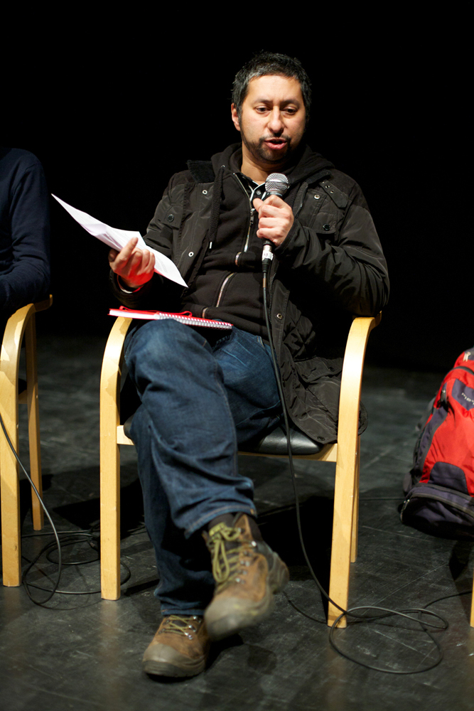 Sacha Kahir sits and holds paper and a mic during a discussion