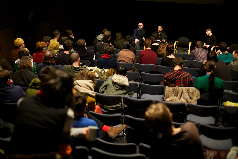The back of the audience is seen looking at the panel during the discussion