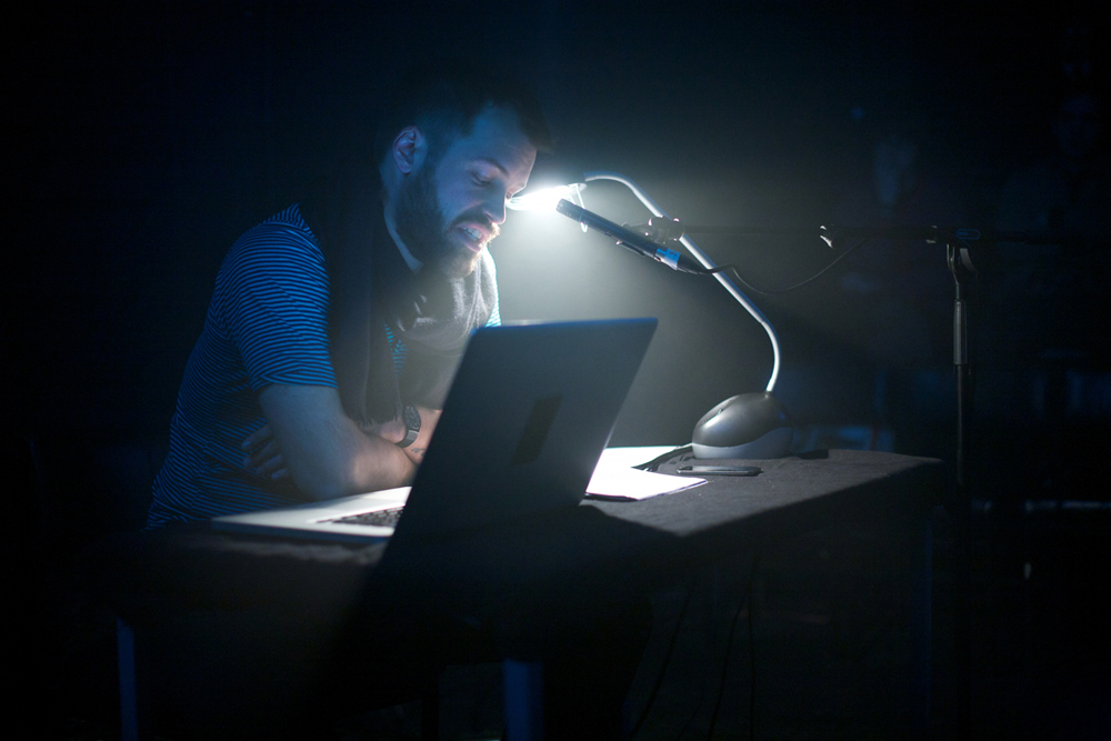 Evan Calder Williams behind a desk in dark foggy space illuminated by lamp