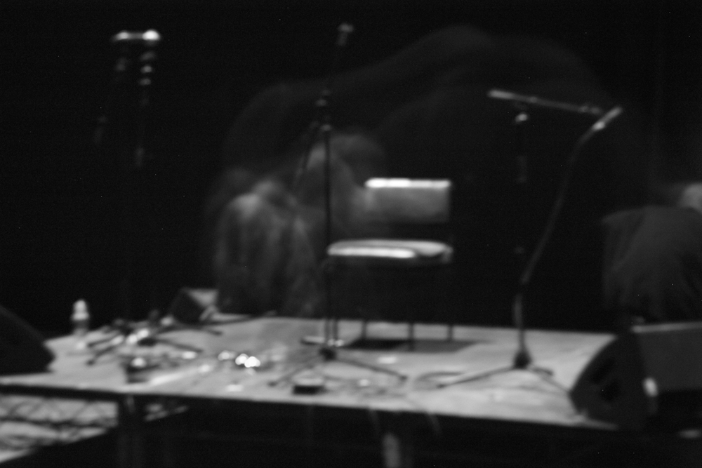 A spectral Keiji Haino hardly visible on stage in near darkness