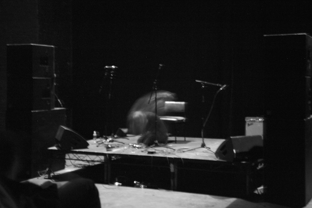 A spectral form performs on a stage, in a very dark room. A B&W picture