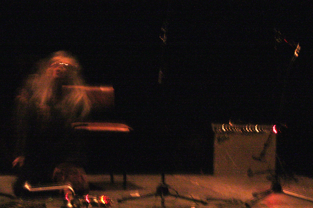 A spectral form performs on a stage, in a very dark room