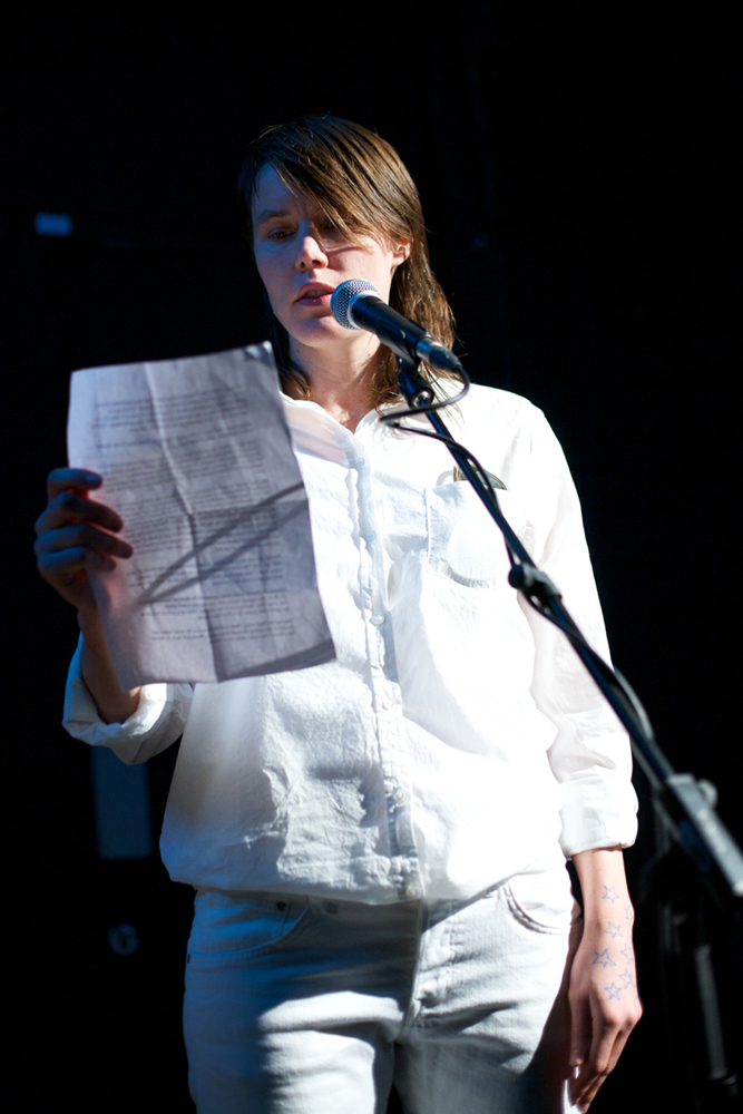 Malin Arnell in white clothes stands and reads from a paper