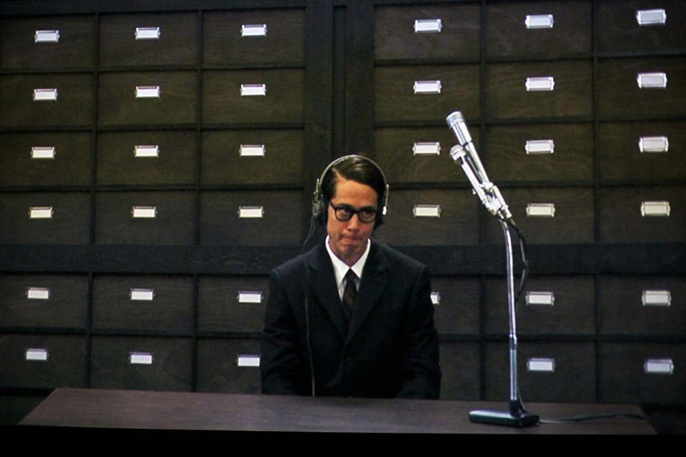 A shot of a screen showing an old office with a character in a suit at a desk