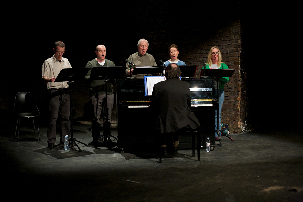 Five choir members sing stage right next to an upright piano
