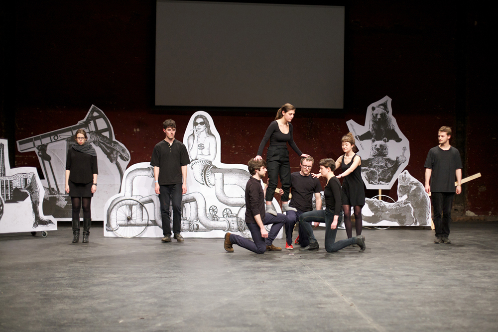 The stage has large paper figures, the ensemble cast help someone to climb
