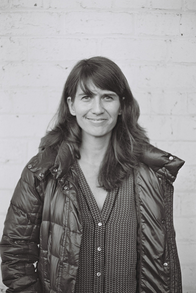 Danielle Goldman smiles in front of a white brick wall