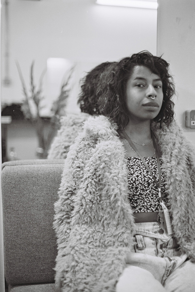 Kia Labeija in a furry jacket sits on a sofa posing for a portrait