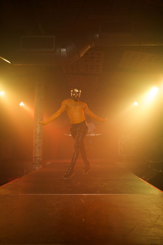 Pony Zion Garcon bathed in gold light walks down a runway in a gold mask