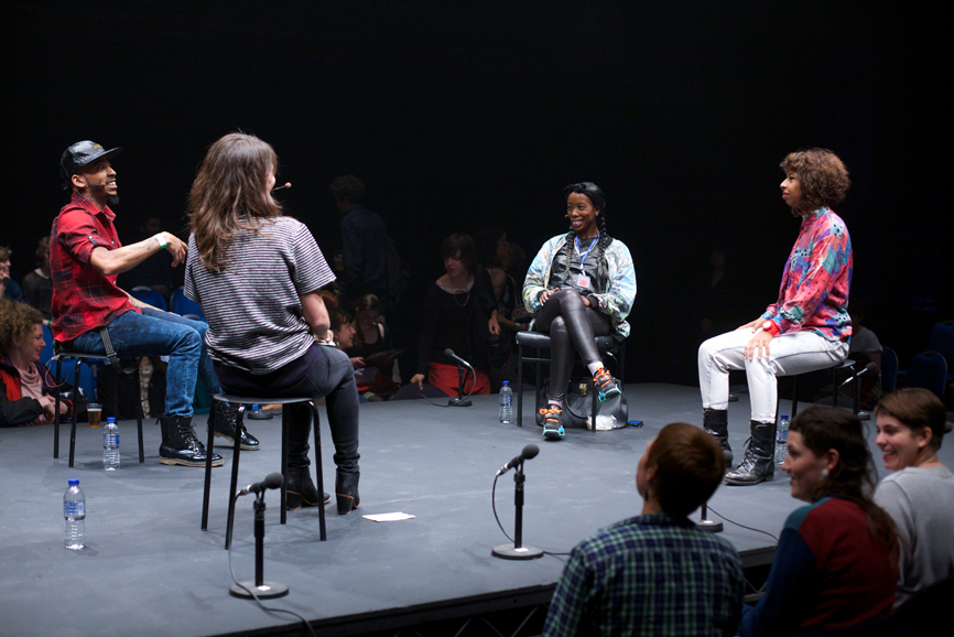 four people sit on a stage looking at each other and smiling