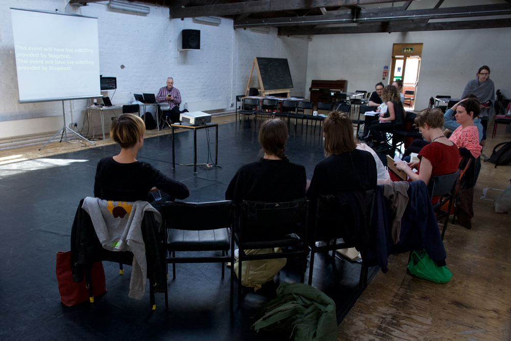 People gather in a semi circle around a screen in a bright room