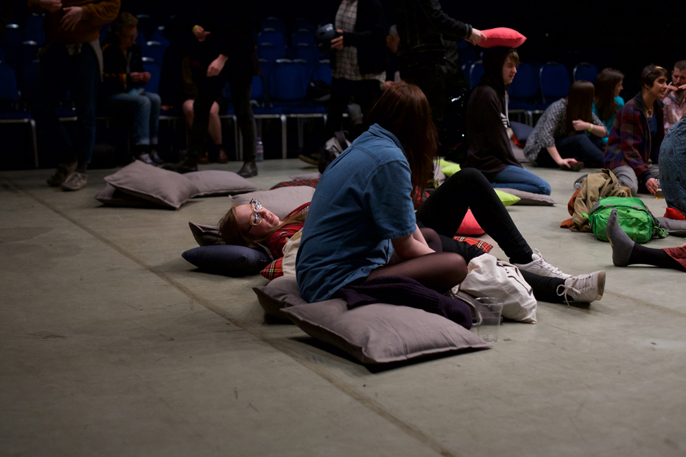 Audience members sit on cushions on a grey floor