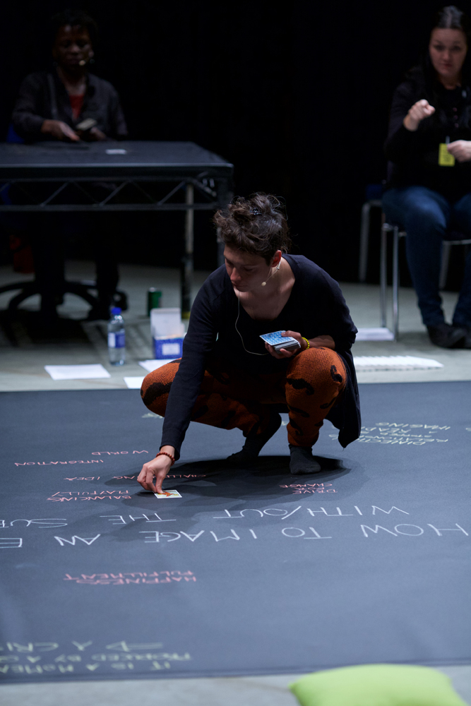 Valentina kneels as she places a tarot card on a chalked word map on the floor