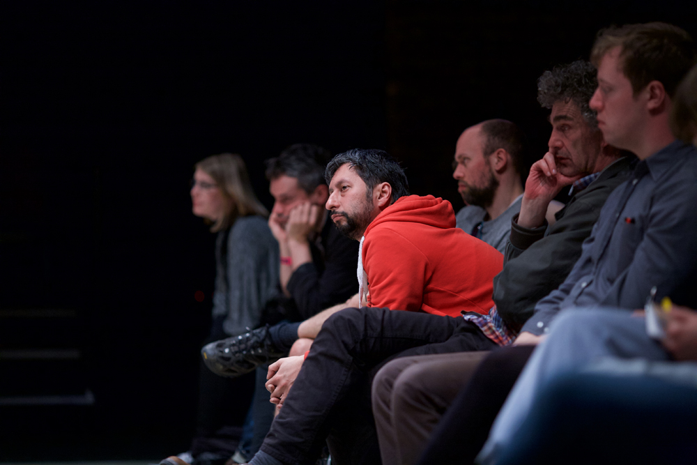 An audience member in a red top leans forward as they listen