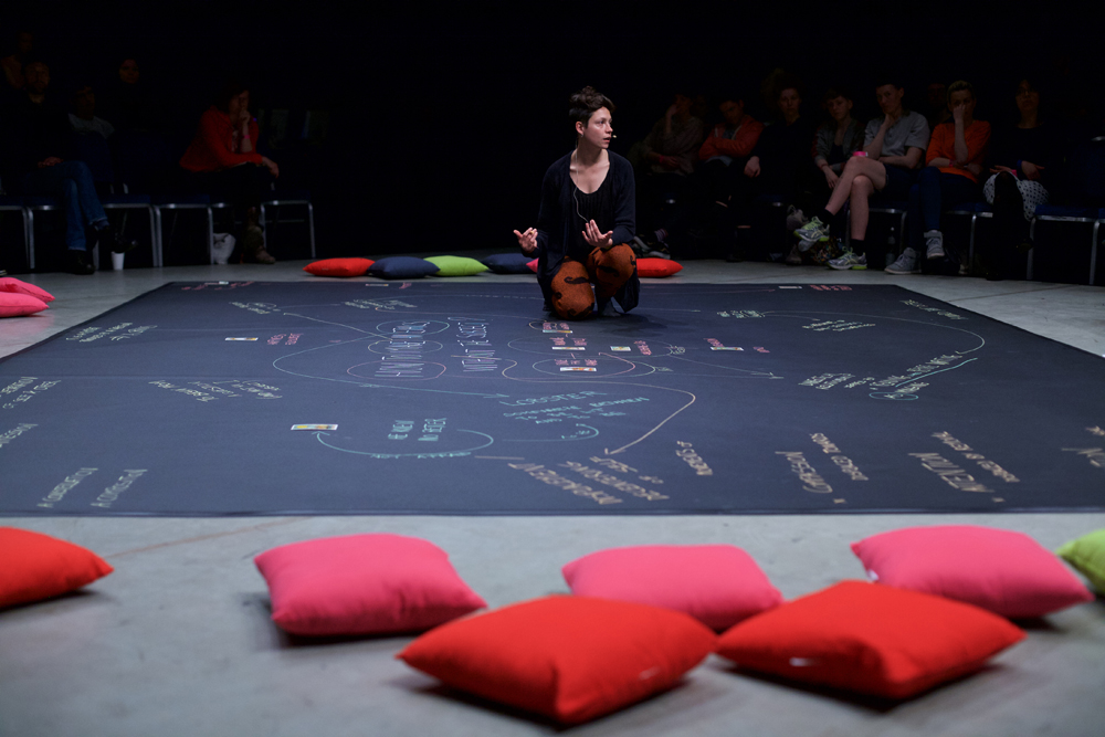 Valentina kneels on a map of words and links written in chalk on black lino