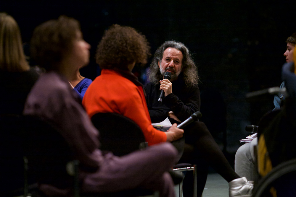 Peter Pal Pelbart speaks into a microphone whilst leaning around some others