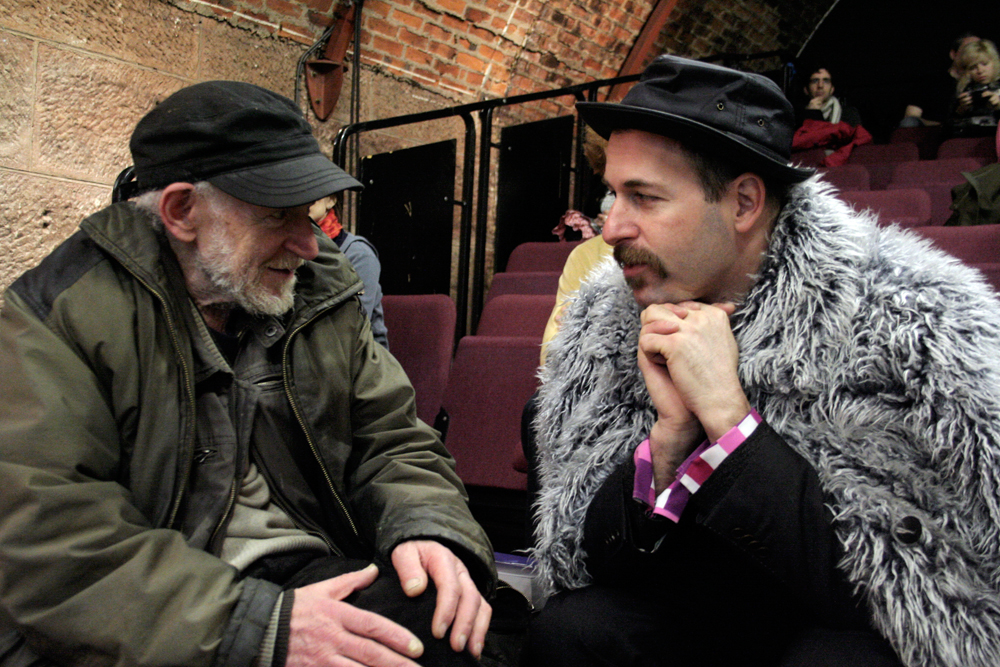 Gustav Metzger in a green jacket and Kenneth Goldsmith in a furry one chat