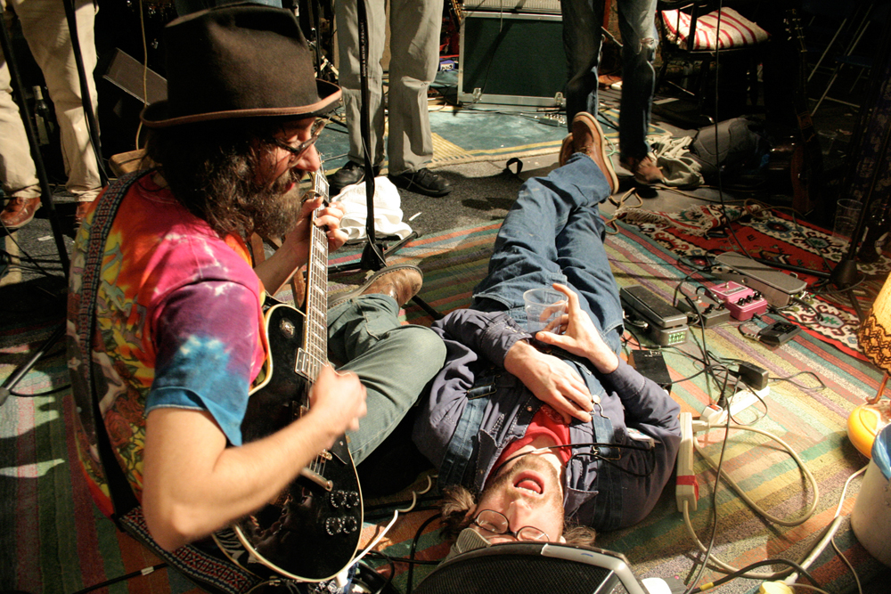 one band member is sprawled on the floor as other gather around