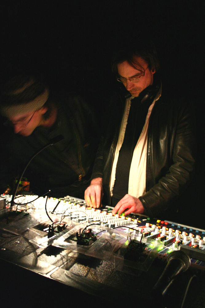 Two Bain brothers look down at a lit mixer in a dark space