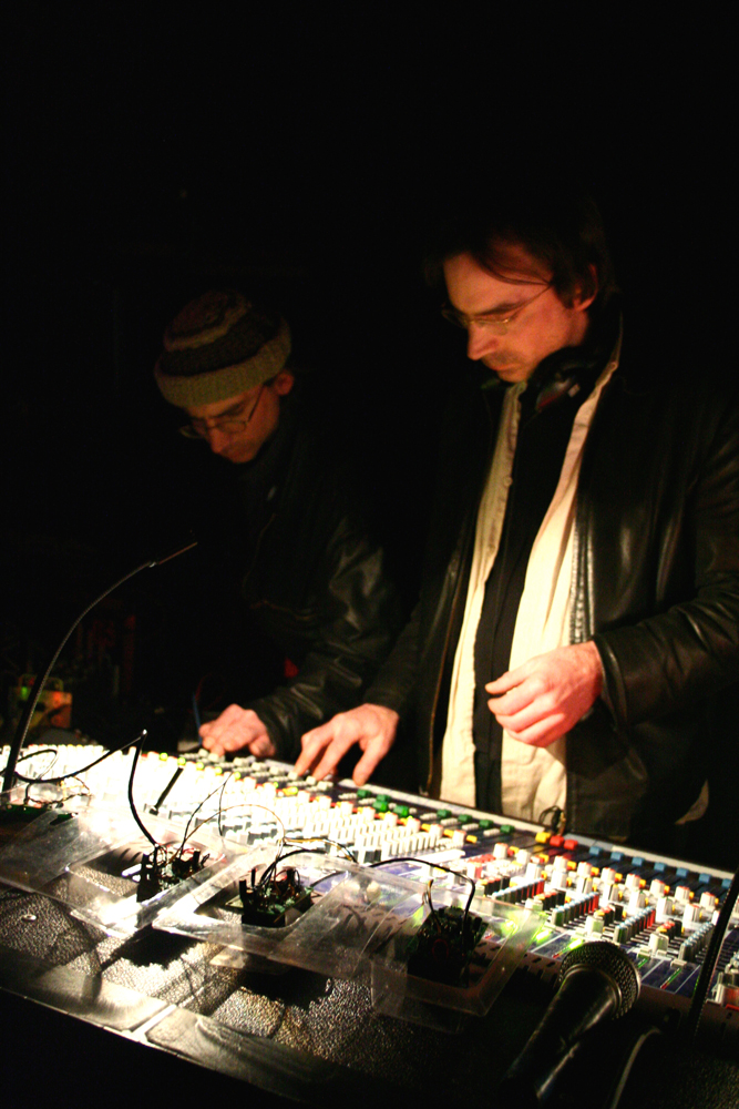 Two Bain brothers look down at a lit mixer in a dark space