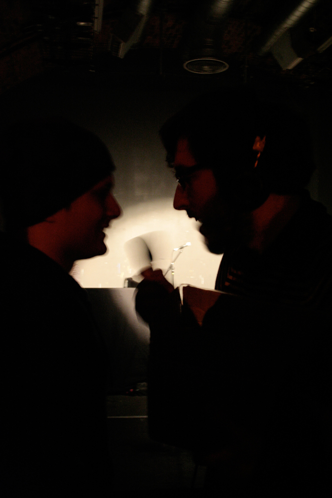Two profiled faces in silhoutte talk, a blurred hand mic between them