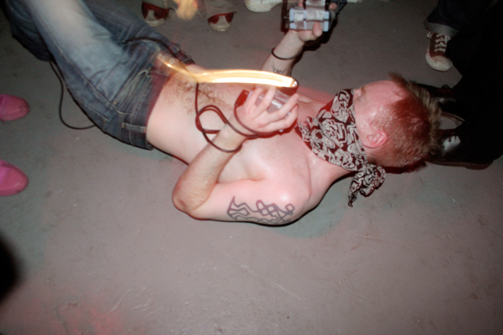 A bare chested man with a bandana of their face writhes on a floor with a torch