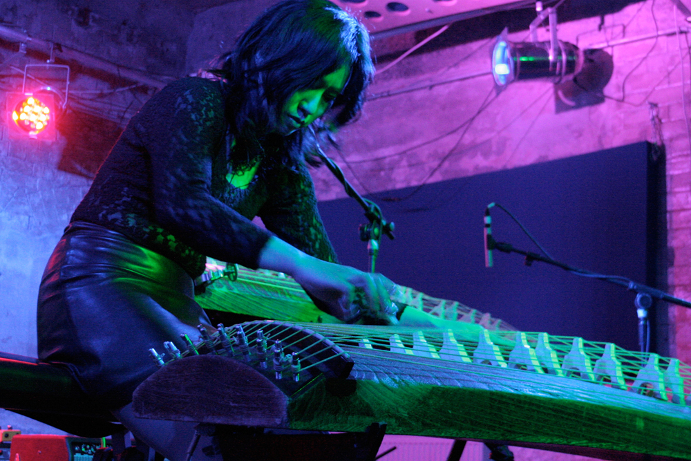 Michiyo Yagi is bent over a large koto stringed instrument in a pink light